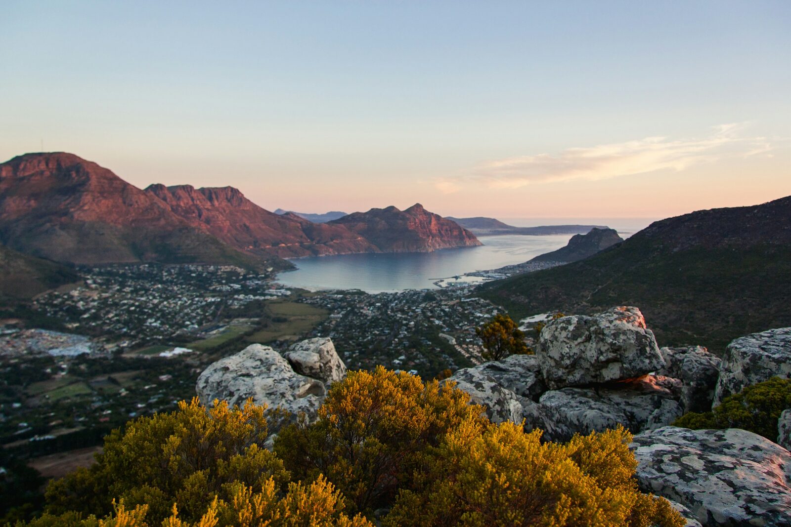 The mountains around Hout Bay glowing at sunset above the harbour and the sea.